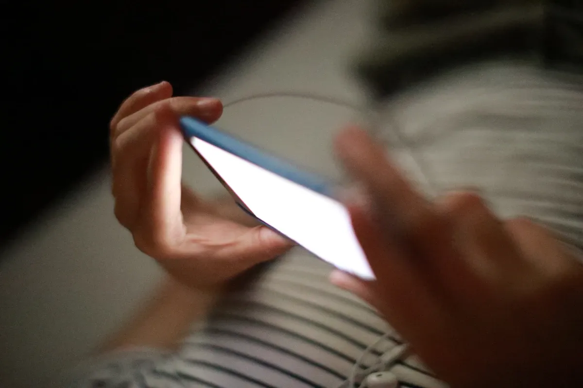 Person scrolling a glowing smartphone screen alone in a dark room at night